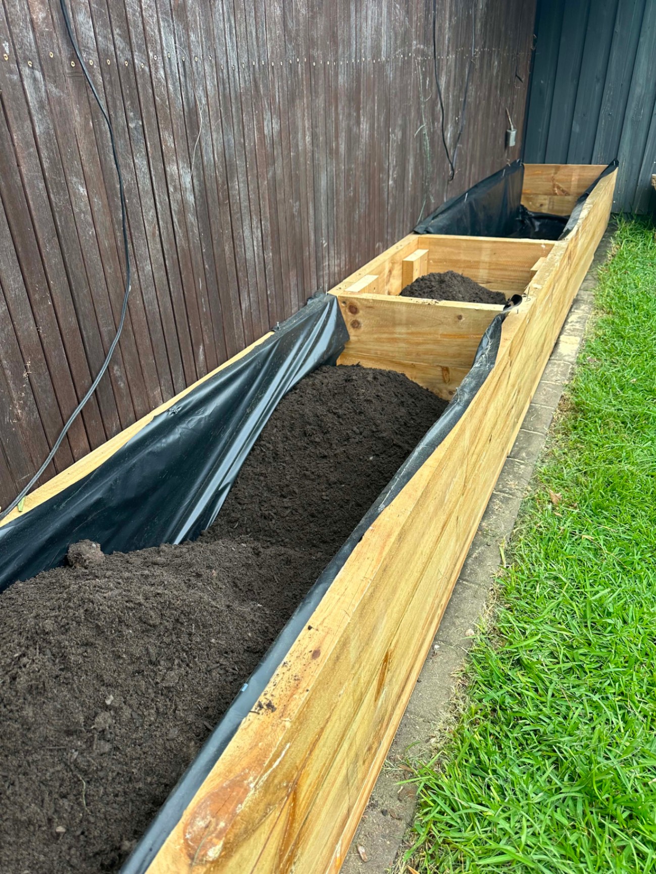 Timber-sleeper raised garden bed alongside a fence